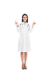 Full length view of doctor in white coat with stethoscope holding pills isolated on white