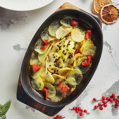 Fish Baked Under Sliced Potatoes in Metal Cooking Pot Top View