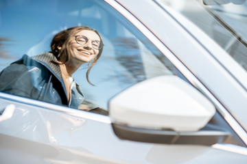 Reflection on the car window of a young stylish woman standing near the car outdoors