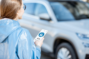 Woman unlocking car using mobile application on a smart phone. Concept of a remote control and car protection through the internet