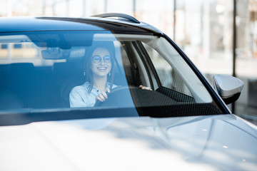 Young and happy woman driving a luxury car in the city, front view through the windshield - Powered by Adobe