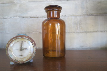 Old antique watch or clock with a brown glass bottle on a wooden table, perfect for some medicinal liquids