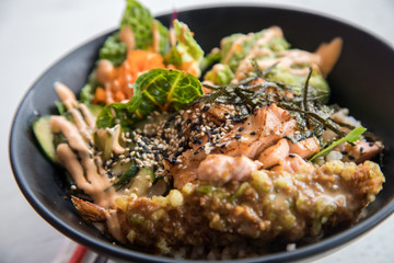 Poke Bowl mit flambierten Lachs, Tempura Shrimp, Guacamole, Masago Kaviar, Salat, Nori Algen und Sesam auf Reis in schwarz Porzellan Schale