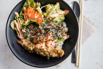 Poke Bowl mit flambierten Lachs, Tempura Shrimp, Guacamole, Masago Kaviar, Salat, Nori Algen und Sesam auf Reis in schwarz Porzellan Schale
