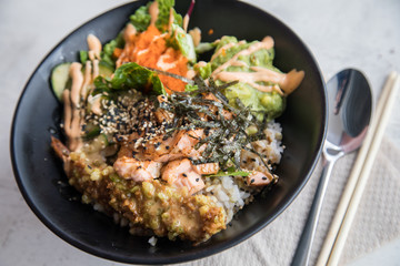 Poke Bowl mit flambierten Lachs, Tempura Shrimp, Guacamole, Masago Kaviar, Salat, Nori Algen und Sesam auf Reis in schwarz Porzellan Schale