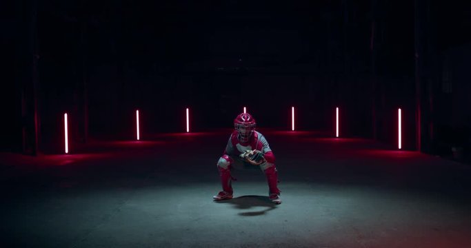 WIDE FIXED Caucasian professional baseball player catcher posing against dark background in a large abandoned warehouse. 4K UHD 60 FPS SLOW MOTION