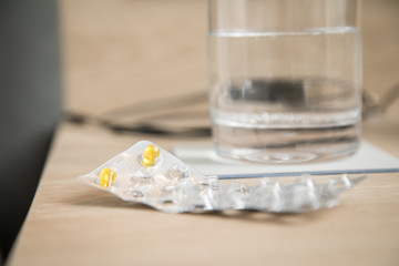 Pillen Blister mit gelben Tabletten und Wasser Glas auf Holz Nachttisch