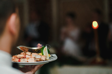 Young man holds a plate of grilled fish over his hand.