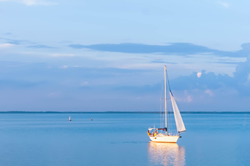 Fototapeta premium Cherkasy, Ukraine - 07.20.2018: beautiful view of boat sails and casts orange glowing reflection at blue sky on river