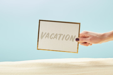 cropped view of woman holding card with vacation lettering in hand isolated on blue