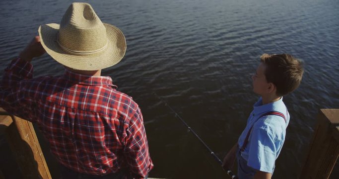 Back view on the teen boy with a grandpa fishing on a big lake and boy pointing at some place. Outdoors.