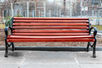 red wooden bench with black iron armrests on the background of the park.