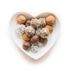 Homemade energy bites, vegan chocolate truffle with cacao and coconut flakes in plate as heart. Concept healthy food.