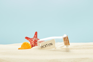 Fototapeta na wymiar glass bottle with vacation lettering on paper near seashell and starfish isolated on blue