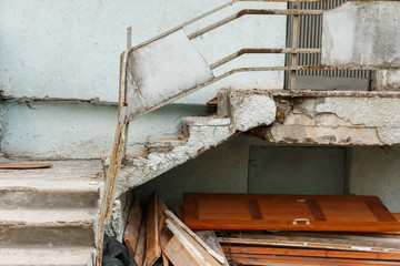 old outdoor staircase in disrepair with peeling paint and pieces of concrete and wooden debris beneath it.