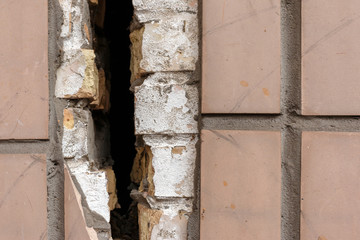 Close-up of tiled wall with a large crack, selective focus. old broken wall with a deep crack, the building must be renovated.