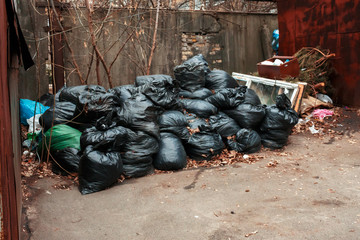 black bags of construction garbage lie between two garages in the yard. garbage bag black bin waste background.