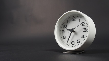 White Alarm clock with hour hand and second hand on black background.