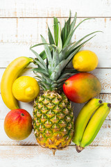 Variety of tropical fruits pineapple mango bananas lemons on white planked wood table. Healthy diet vitamins concept. Poster Banner Template. Flat lay