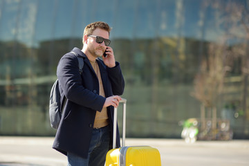 Middle age man with suitcase using smartphone with railway station on  background.