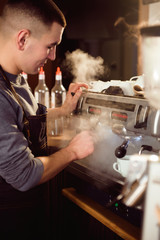 Smiling male barista using professional coffee machine enjoying job in cafe improving skills of making cappuccino