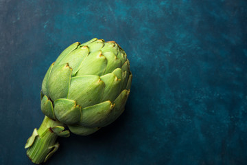 Fototapeta premium Ripe green artichoke on dark blue background. Creative food poster. Minimalist style. Mediterranean Spanish cuisine healthy plant based diet superfoods concept