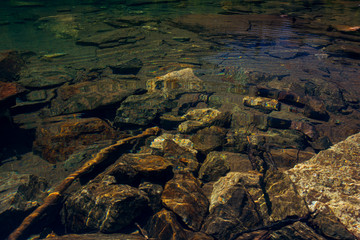 Crystal-clear water in the high-mountainous lake of Baduk with stones at the bottom on a summer day.