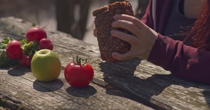 Female hands cutting a slice of wholemeal bread at a table in the outdoors