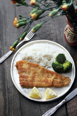 Fish in breadcrumbs fried in oil with rice and broccoli.