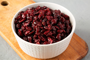 Dried cranberries in a bowl on rustic wooden board over gray background, side view. Close-up.