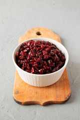 Dried cranberries in a bowl on rustic wooden board over gray surface, low angle view.