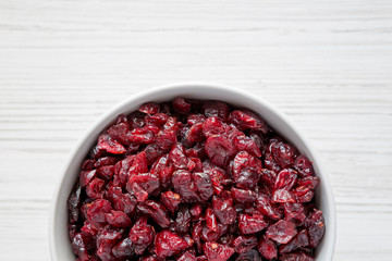 Dried organic cranberries in a bowl over white wooden background, top view. From above, overhead, flat lay. Copy space.