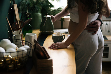 Beautiful young, stylish pregnant girl with her husband cook cocoa with marshmallow in the kitchen in a beautiful interior