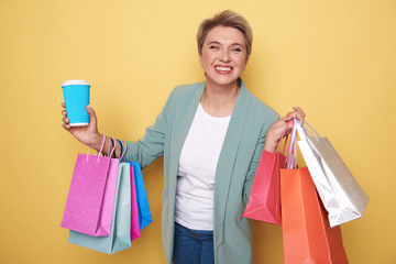 Happy woman looking at camera and holding colorful shopping bags and cupholder