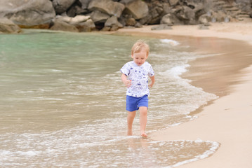 Little blond boy running on the water along the sea beach