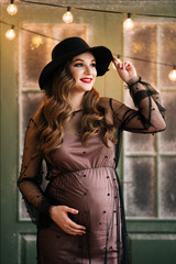 Beautiful young, stylish pregnant girl, in a black dress and hat, in the interior of a French bakery