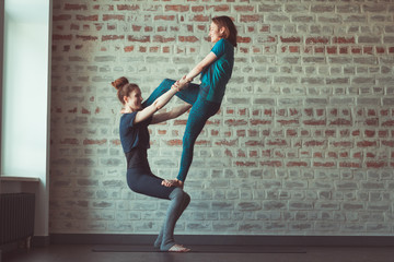 two beautiful caucasian women doing partner yoga in yoga studio opposite brick wall