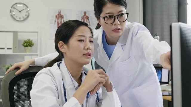 Doctor and nurse examining patients medical records on computer discussing. healthcare worker team working in hospital office. young girl standing next to colleague talking pointing finger on screen