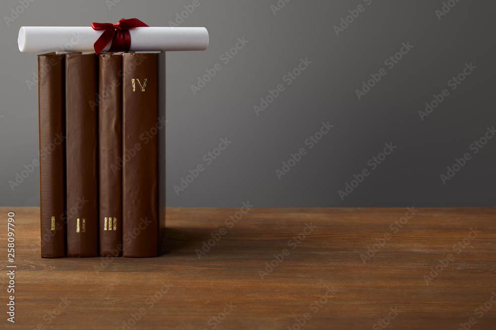 Poster Brown books and diploma with red ribbon on wooden surface on grey - Posters