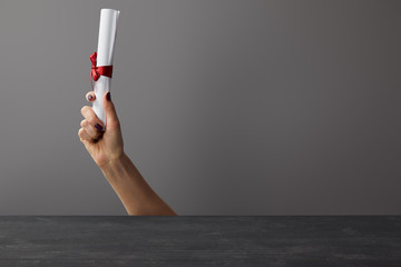 Cropped view of woman holding diploma with red ribbon on grey