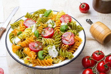 Italian food - Salad with colorful pasta, cherry tomatoes, feta cheese and fresh basil on white wooden background