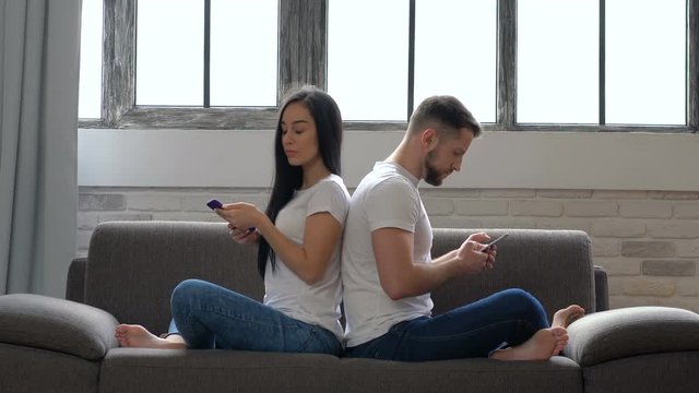 Modern couple sitting on the sofa back to back. No emotional, dont talking. Looking on each ather from back. Couple problems. Communication problems.