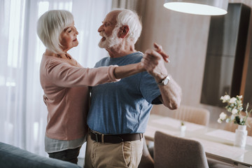 Joyful gray haired couple dancing in living room