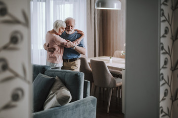 Positive elder couple embracing in living room