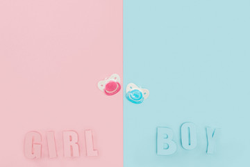 top view of pacifiers, boy, girl lettering on pink and blue background with copy space