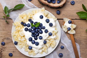Obraz na płótnie Canvas Tasty pasta with fresh organic blueberries and vanilla cream. Sweet dinner on retro wooden table.