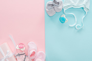 top view of pacifiers, gift, booties, bonnet, socks on pink and blue background