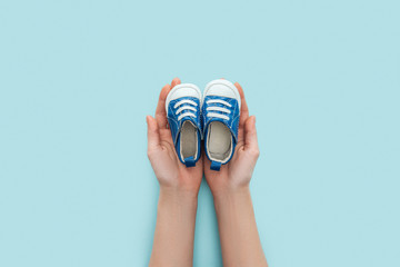 partial view of adult man holding sneakers on blue background with copy space