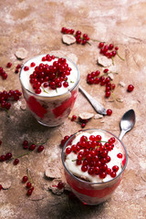 Healthy dessert with organic red currants, fresh yogurt and corn flakes. Dietary breakfast on a brown background