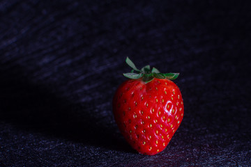 FIRST PLANE OF STRAWBERRY PROJECTING ITS SHADOW ISOLATED IN BACKGROUND WITH BLACK TEXTURES